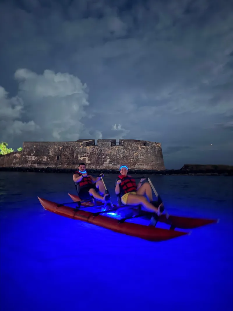 Glowing blue LED water bike crossing the Condado Lagoon at night near the kayak route with the San Juan skyline lit behind, Puerto Rico